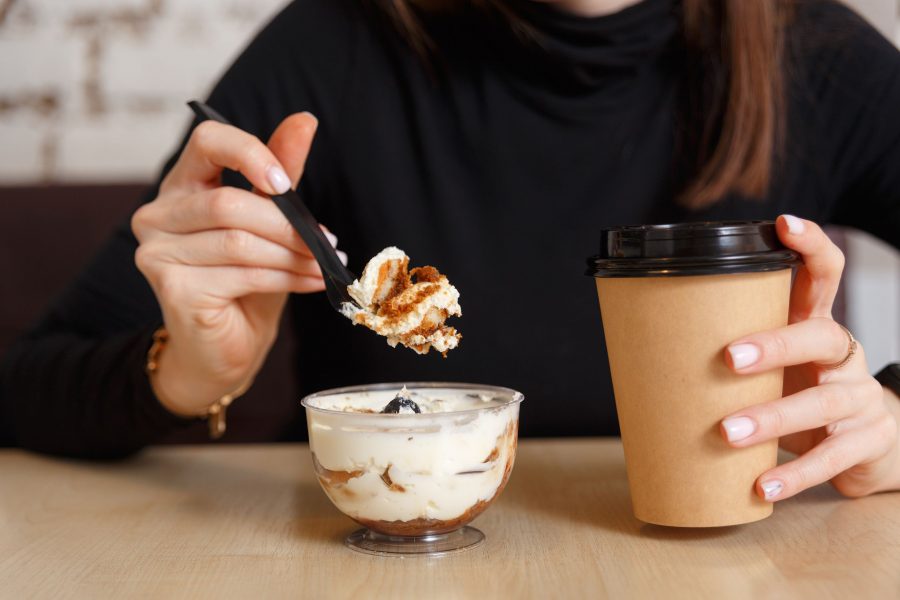 Woman Eats Creamy Dessert And Drinks Coffee At Breakfast In Cafe.