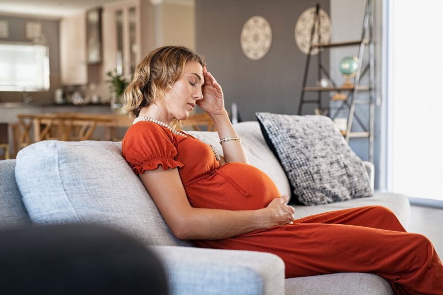 Exhausted middle aged pregnant woman suffering headache sitting on couch in the living room. Stresse