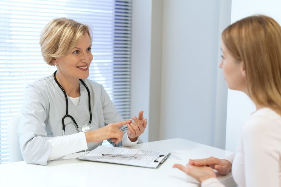 General Practitioner Consulting Female Patient In Clinic At Meeting In Hospital Office. Doctor Talki