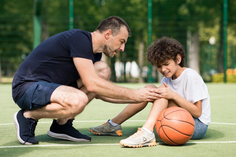 Teacher Helping Boy With Knee Trauma After Playing Basketball