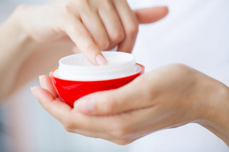 Cropped Image Of Beautiful Young Woman Applying Cream While Sitting On Bed At Home